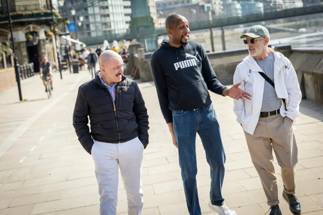 a man talking happily with his 2 other friends walking with them on a roadside