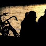 A couple enjoying a peaceful riverside moment, their bicycles parked nearby.