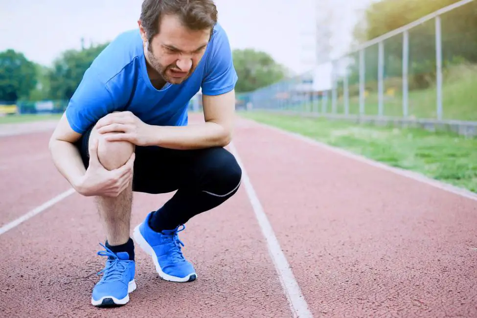 A runner sitting holding his knee in pain