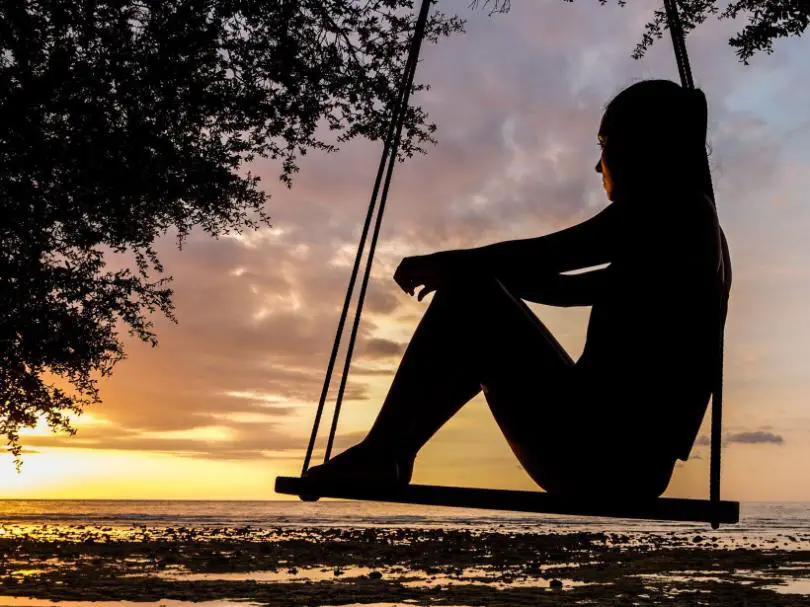 A silhouette of a girl seated on a swing, watching sun set
