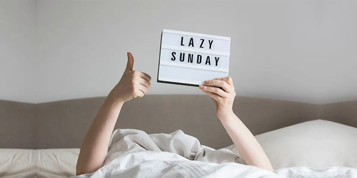 Female hands holding "lazy Sunday" board while in bed