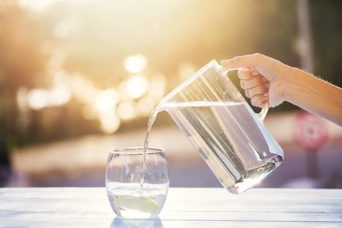 A person pouring water in a glass from a jug