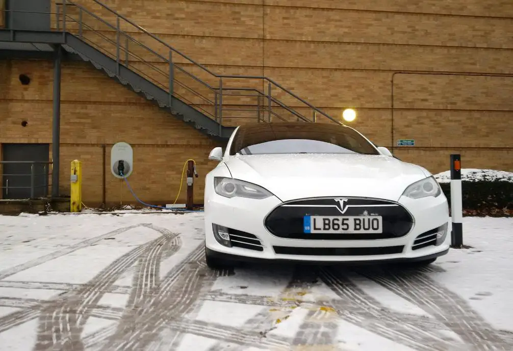A white Tesla parked in cold weather in front of a home charging point 