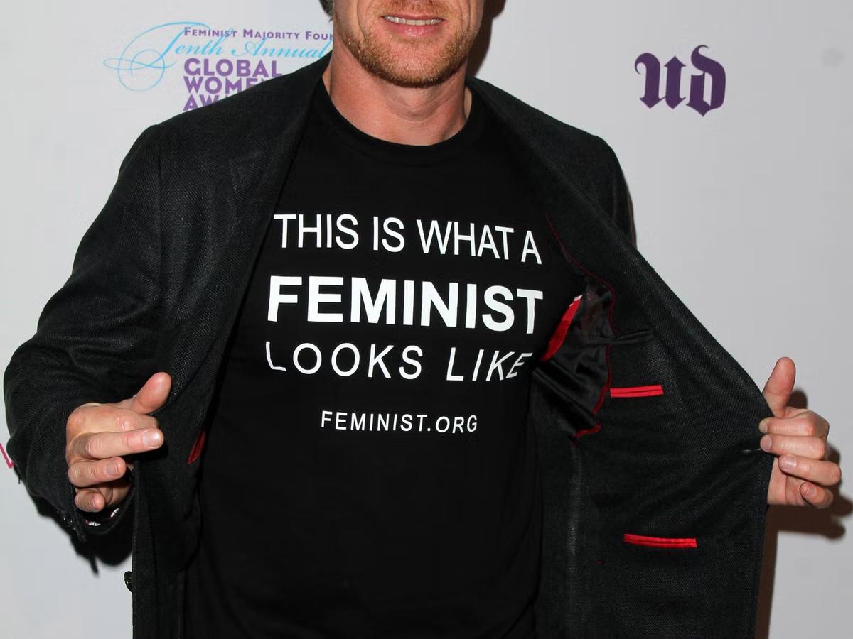 A man showing his inner black shirt that says "This is what a feminist looks like"