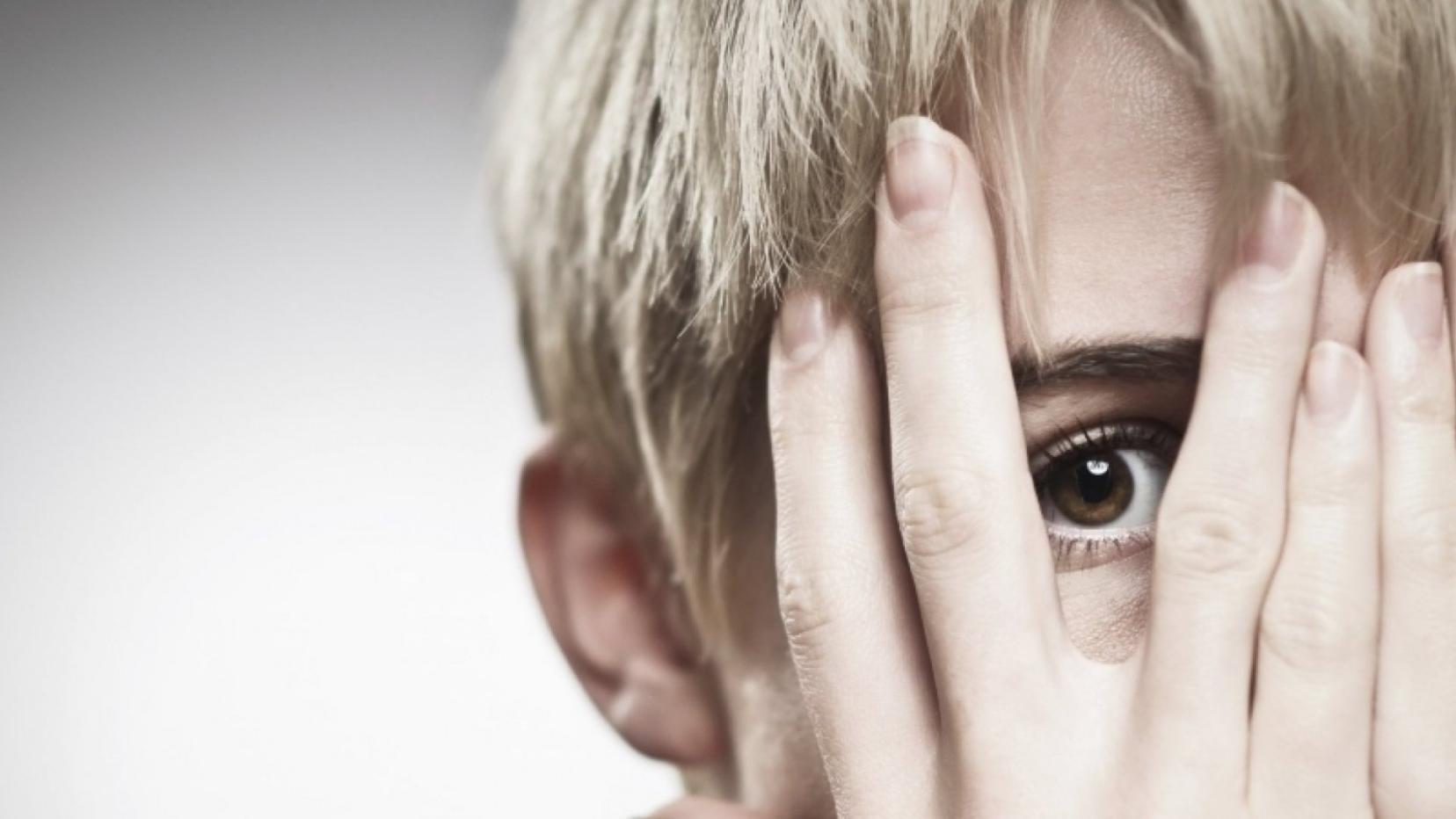 A person hiding his face in his hands just showing his one eye