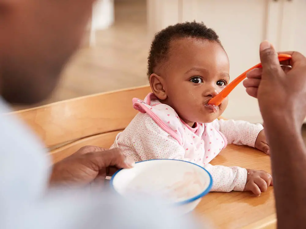  A person is feeding his son with an orange spoon.