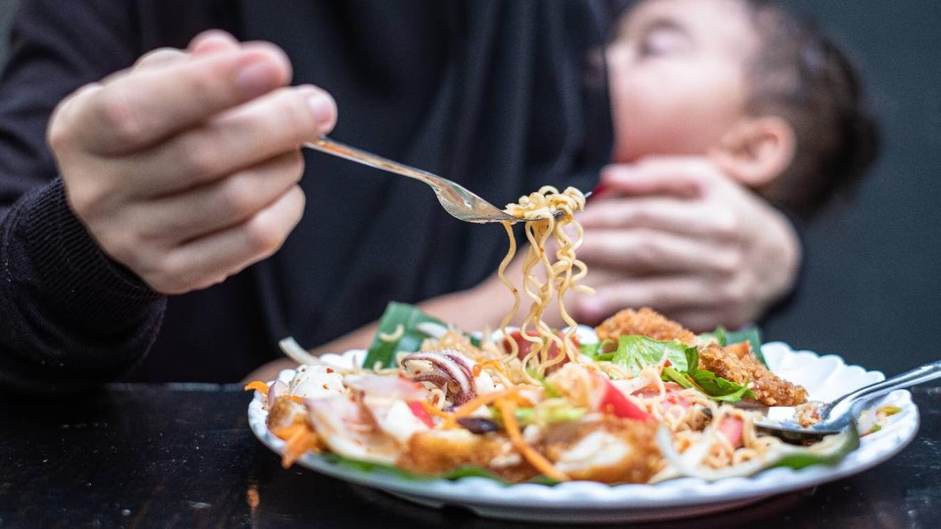 A plate full of spicy food is placed in front of a mother feeding her infant.