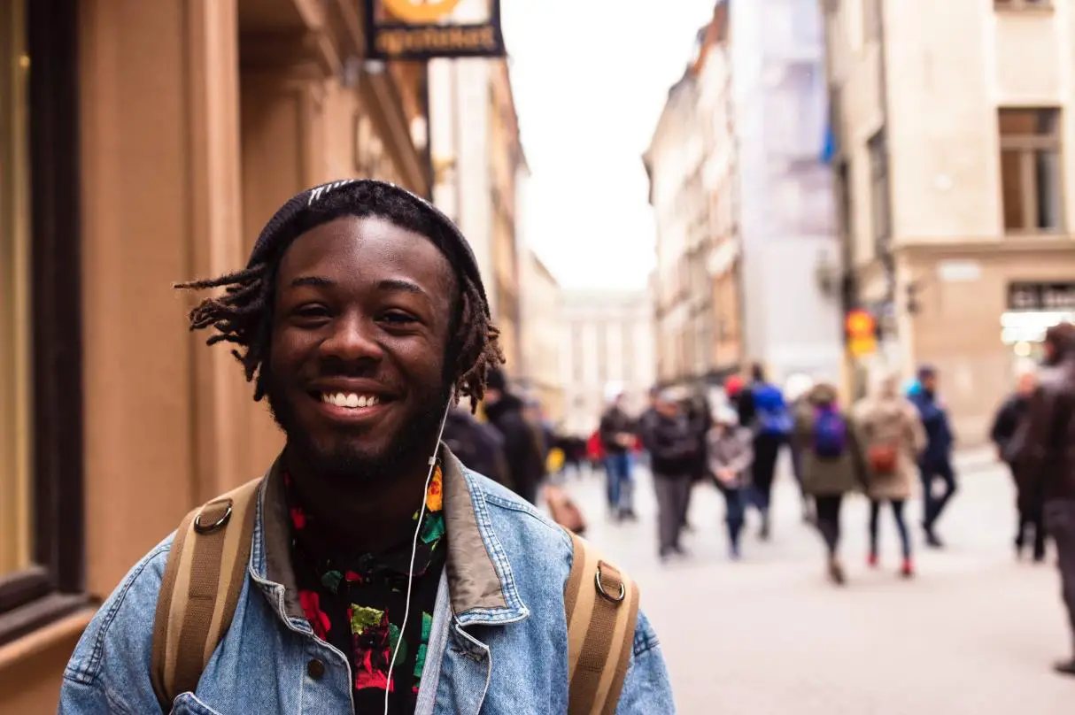 African man smiles confidently into the camera amidst the dynamic backdrop of a bustling urban road, 