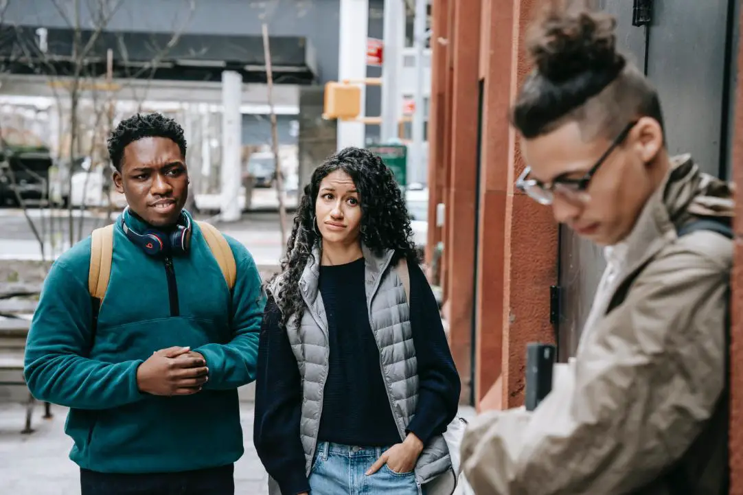 2 persons looking at a 3rd person who is shying from them and looking down