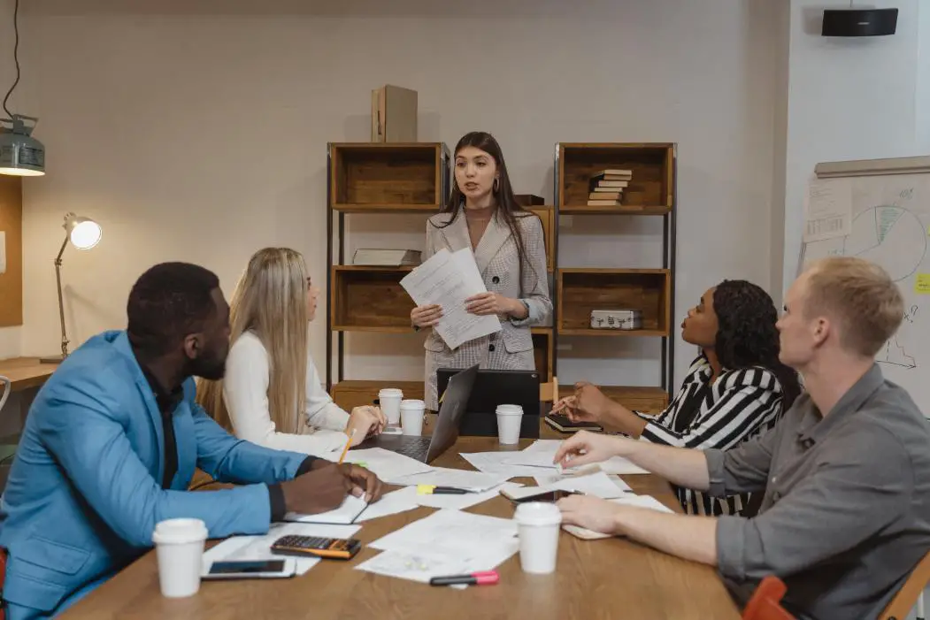 A Woman standing and presenting her office Work in front of her colleagues confidently