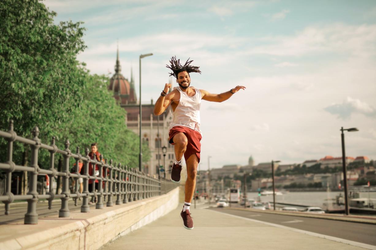A Person wearing shorts on a sideways of a road in a sunny day jumping in excitement fully energetic during his running process 