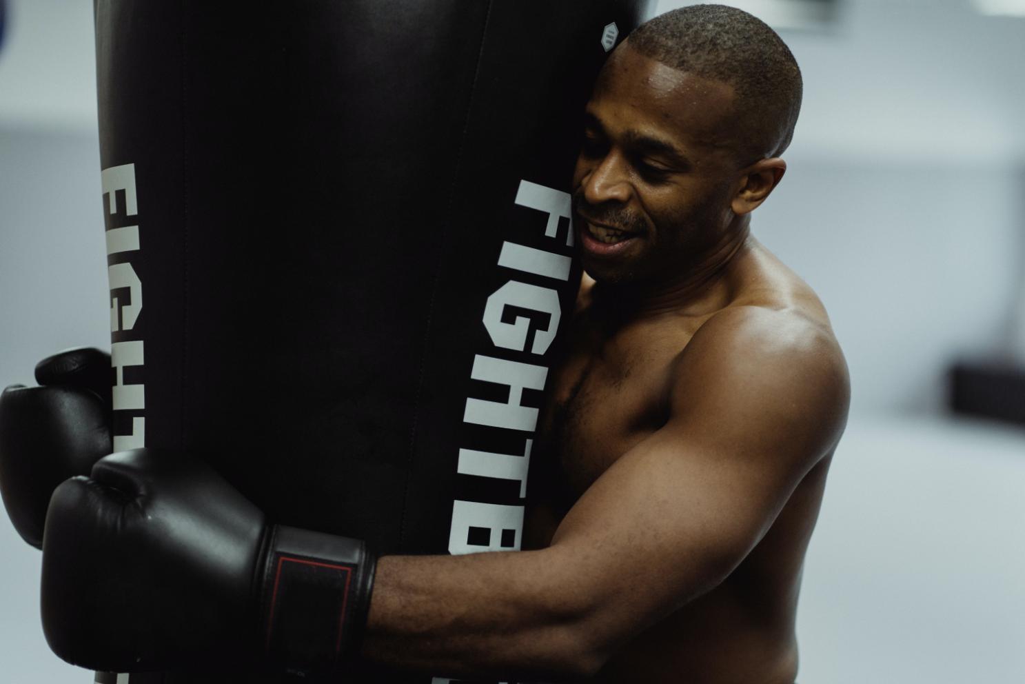 A Man doing his workout with the punching bag , holding it with both hands and looking relieved from stress giving a smile