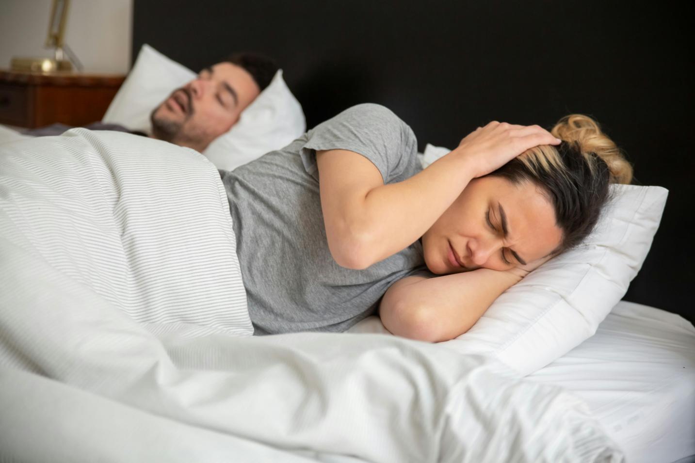 A man snoring while sleeping on his bed- while his wife getting irritated by the noise