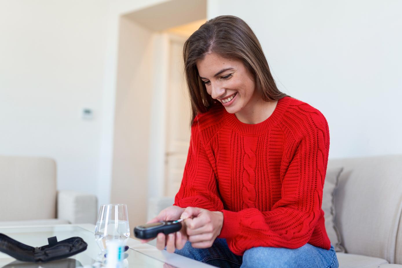 A Woman sitting inside her house testing her blood sugar level with a smile on her face