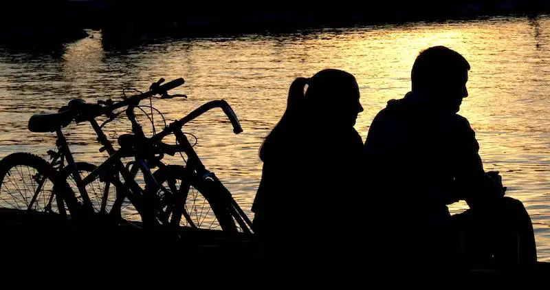 A couple enjoying a peaceful riverside moment, their bicycles parked nearby.