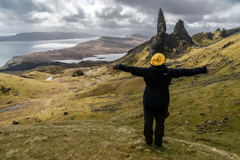 A girl stands alone outside in the mountains, enjoying the moment with both arms open