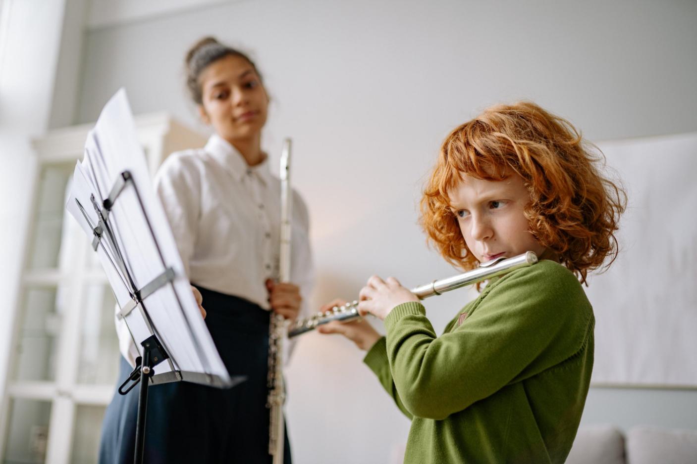 A little kid learning to play Flute in the presence of her teacher