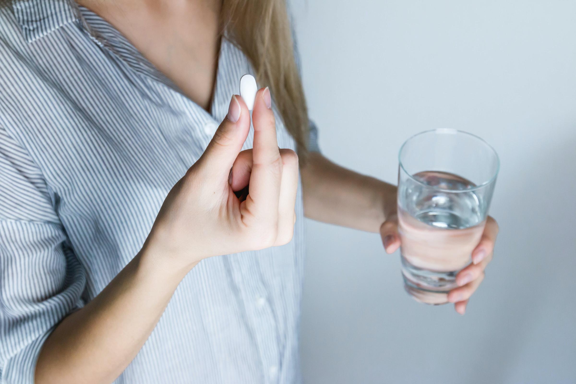 A Girl holding a glass of water and taking the medication