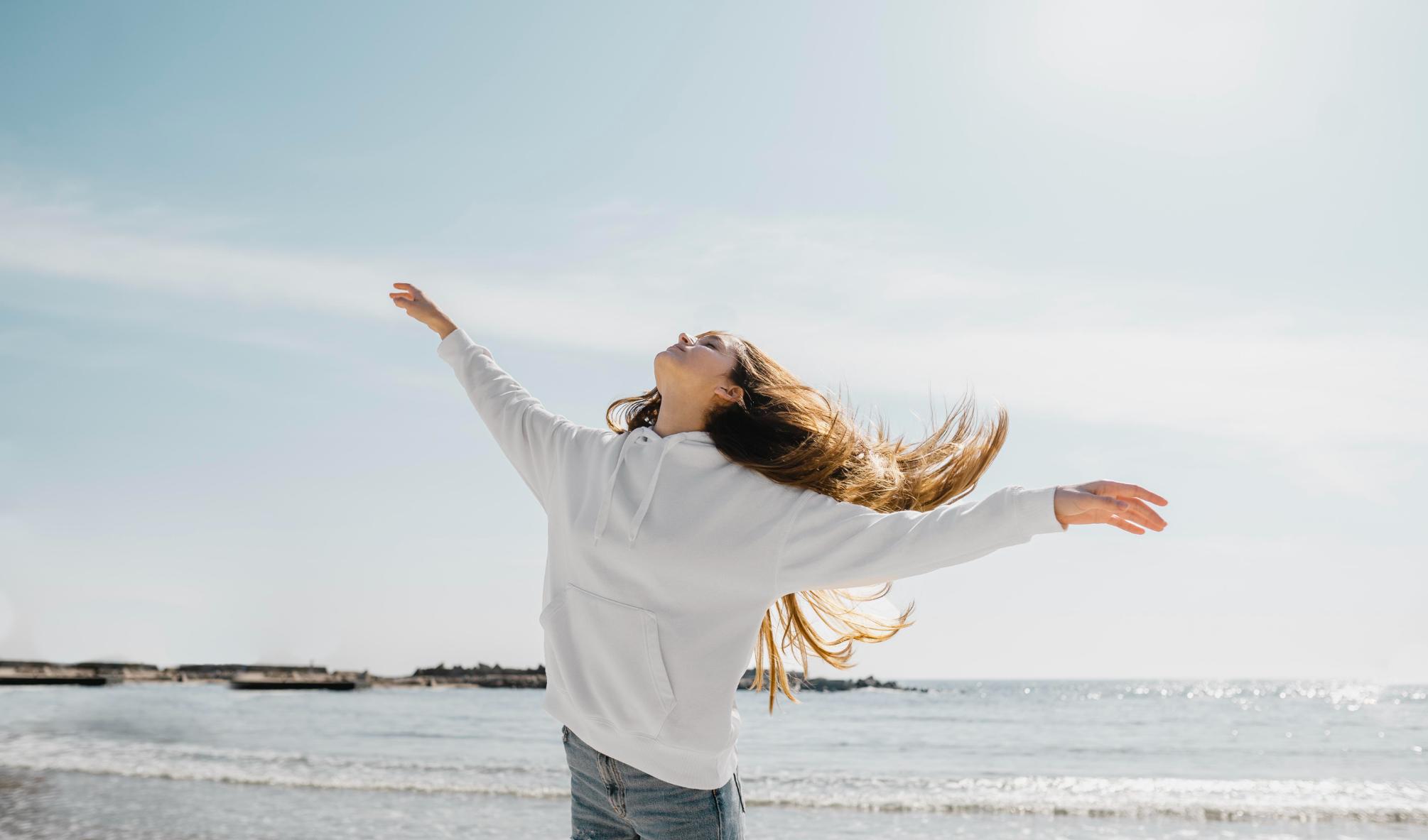 A Woman enjoying with a good mood on a beach with her hands wide open and her face towards the sky