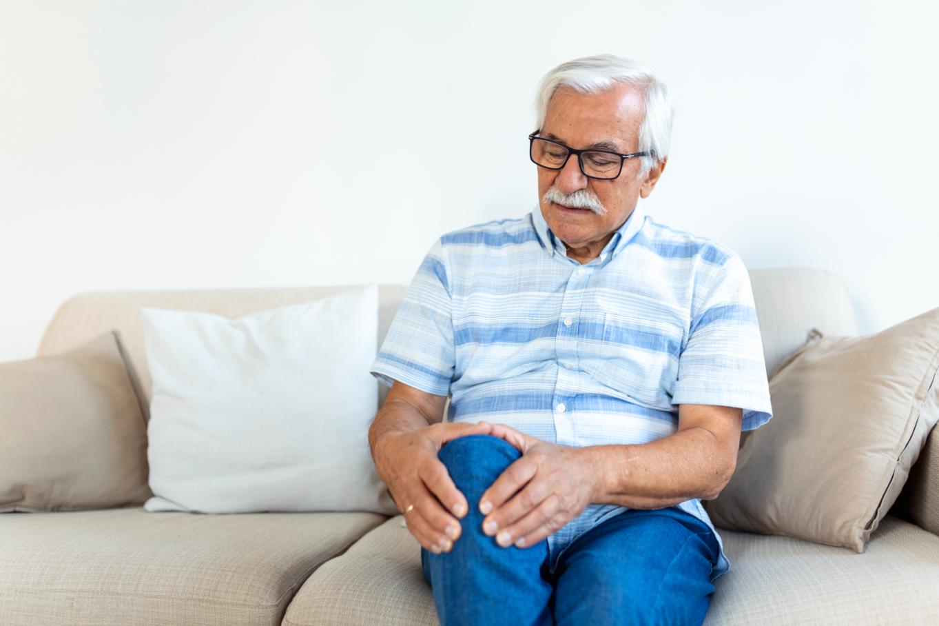 An old man sitting on the sofa holding his knee in pain