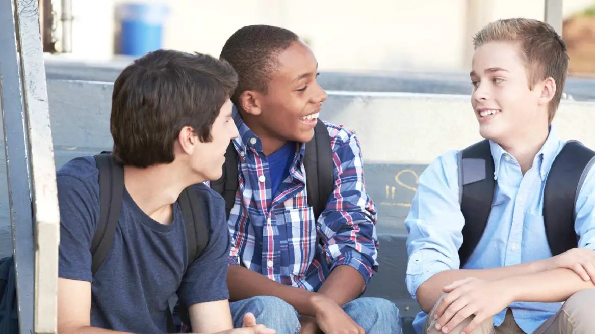 Three boys with backpacks engaged in conversation, sharing laughter...