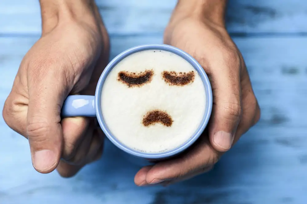 A person wearing a blue shirt holds a coffee mug with a sad expression