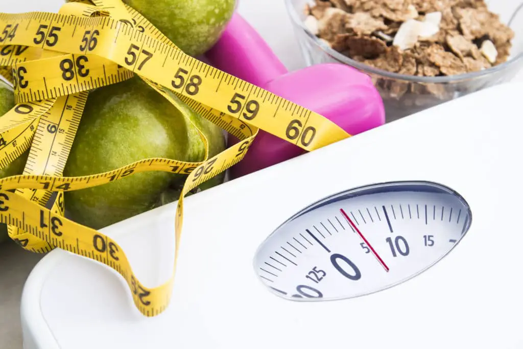 A weighing machine with a measuring tape, positioned next to a variety of food items.