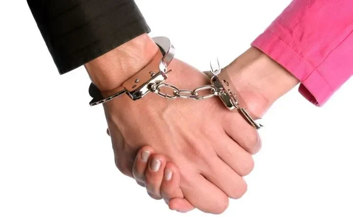 Two joined male and female hands handcuffed together.