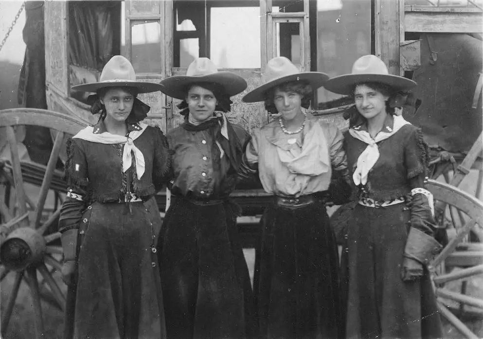 Four Wild West women standing arm in arm with each other, posing for a picture