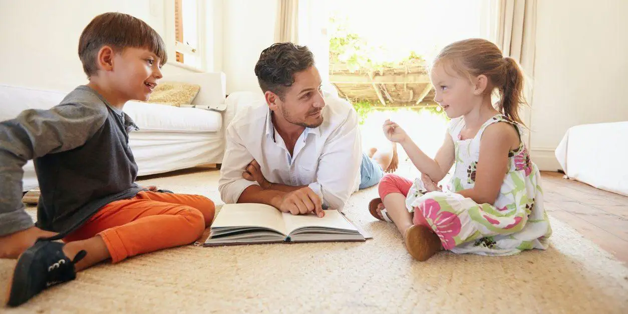 A father engaging in a conversation and teaching his children while sitting together on the floor