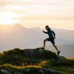 A man gracefully running on a trail, silhouetted against the horizon with the setting sun behind him