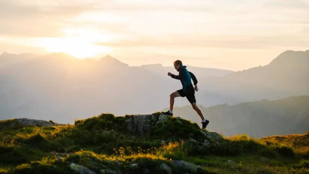 A man running on a trail against the horizon with the setting sun 
