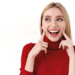 A girl wearing a red turtle neck with a white background, smiling showing her teeth