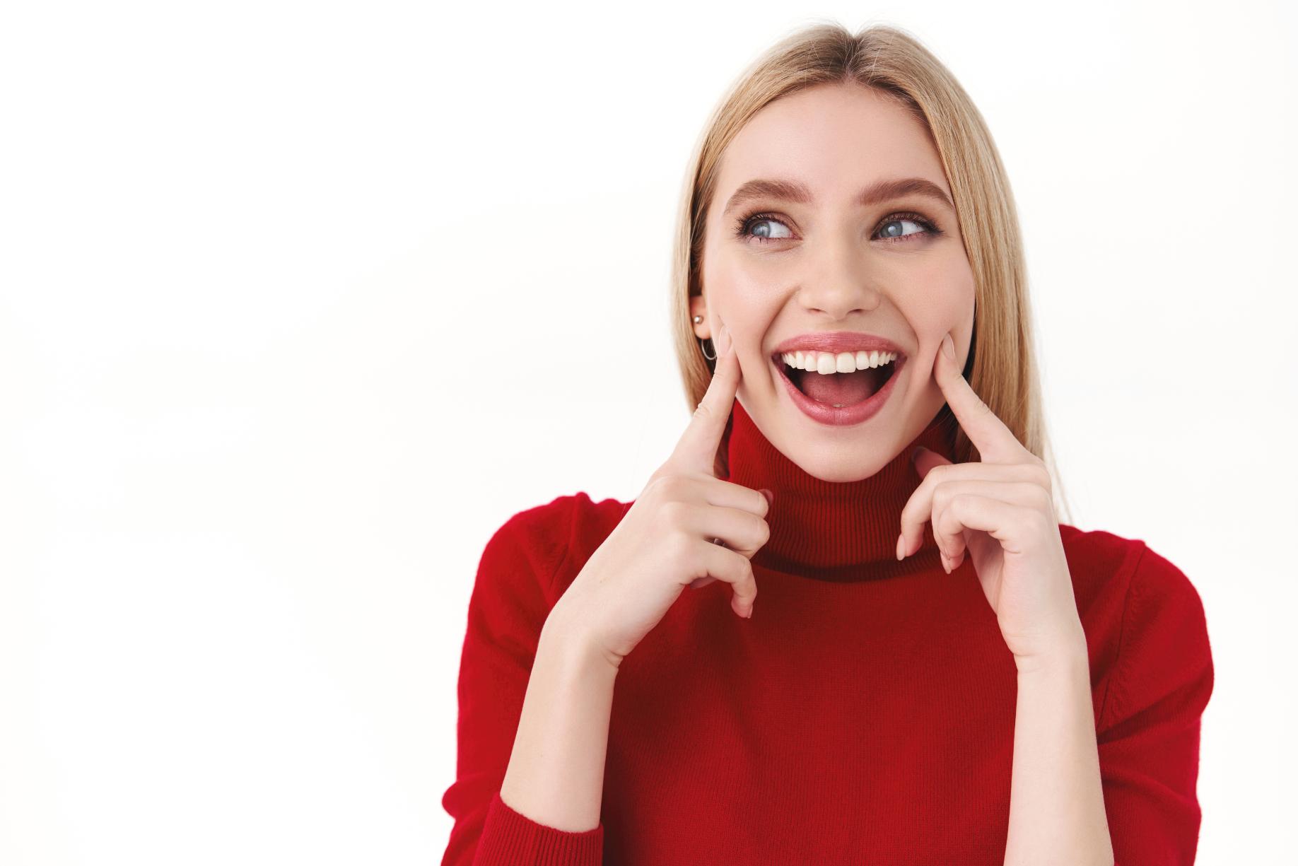 A girl wearing a red turtle neck with a white background, smiling showing her teeth