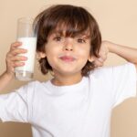 A child holding a glass of milk, trying to show off his muscles