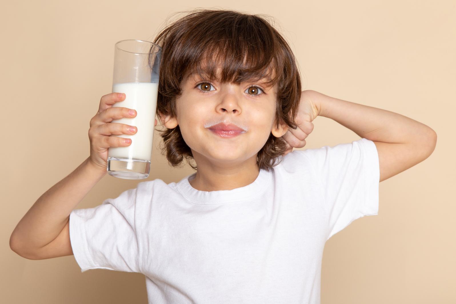 A child holding a glass of milk, trying to show off his muscles