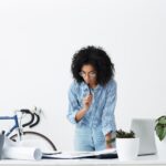 A female standing, touching her her with her lips, trying to focus on the paper put on the table