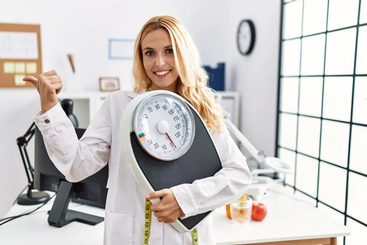 A female nutritionist in her clinic showing a weighing machine and smiling