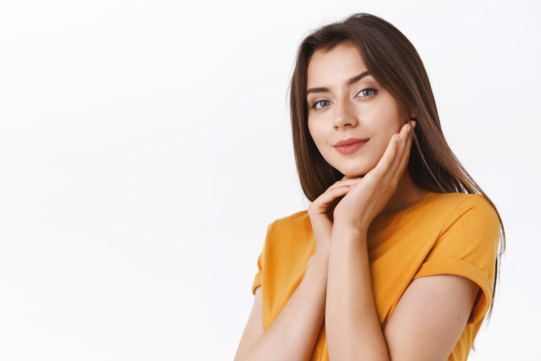 A Young girl wearing a yellow tshirt showing off her glowy skin, keeping her hand below her cheek