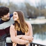 A young couple outside near a lake looking towards each other in a happy mood