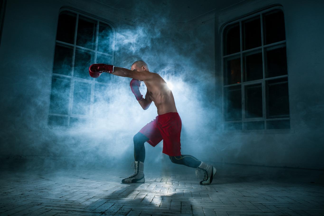 A young athlete practicing shadow boxing and punching in a room with bluish smoke