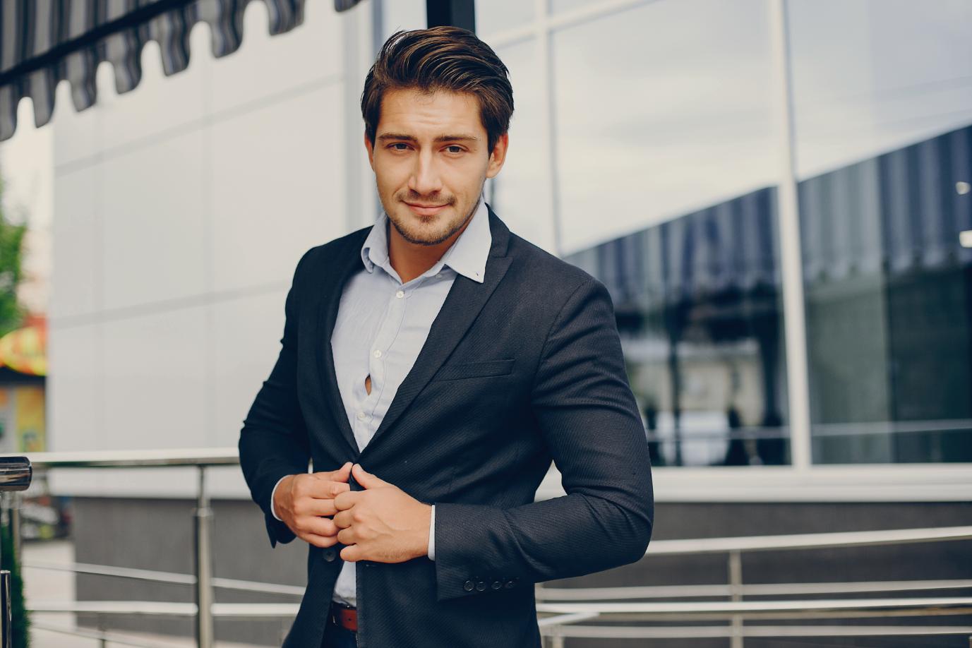 A Young person wearing a suit in front of a large building posing in a confident way