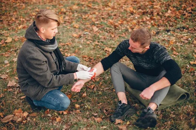 A person helping his friend and providing him first aid, who has an injury on his right hand