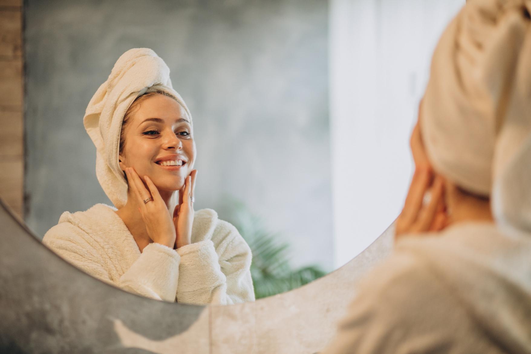 A woman standing in front on the mirror applying face cream for a healthy and glowing skin
