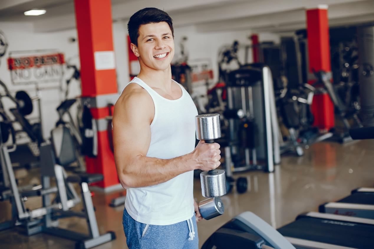 A young Man in a good mood exercising in gym holding a dumbbell