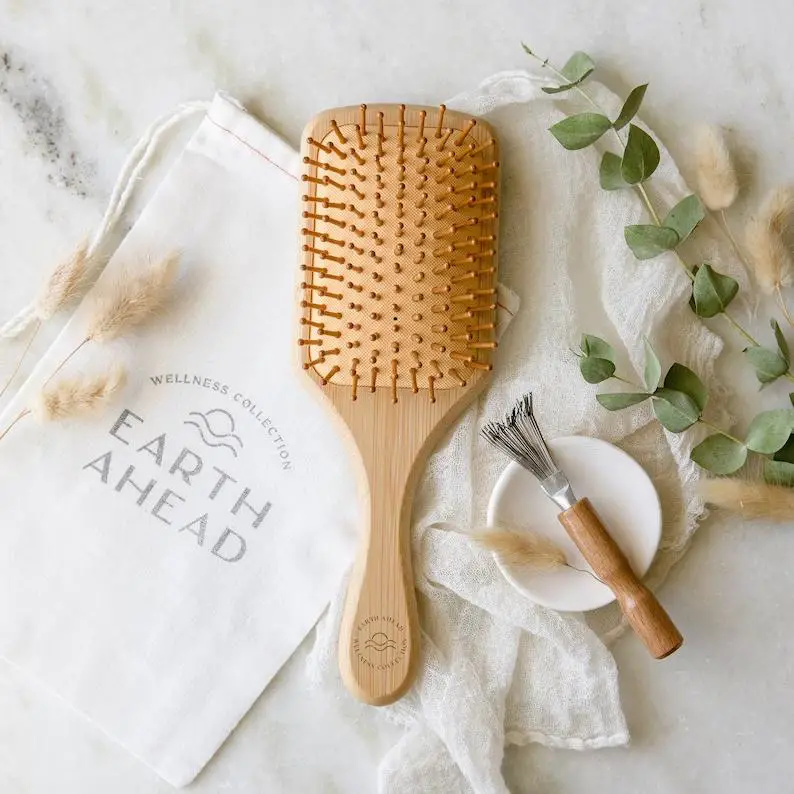 A Bamboo Hair Brush placed on a small pouch against a backdrop of fabric, having 2 green small leafy vines on one side