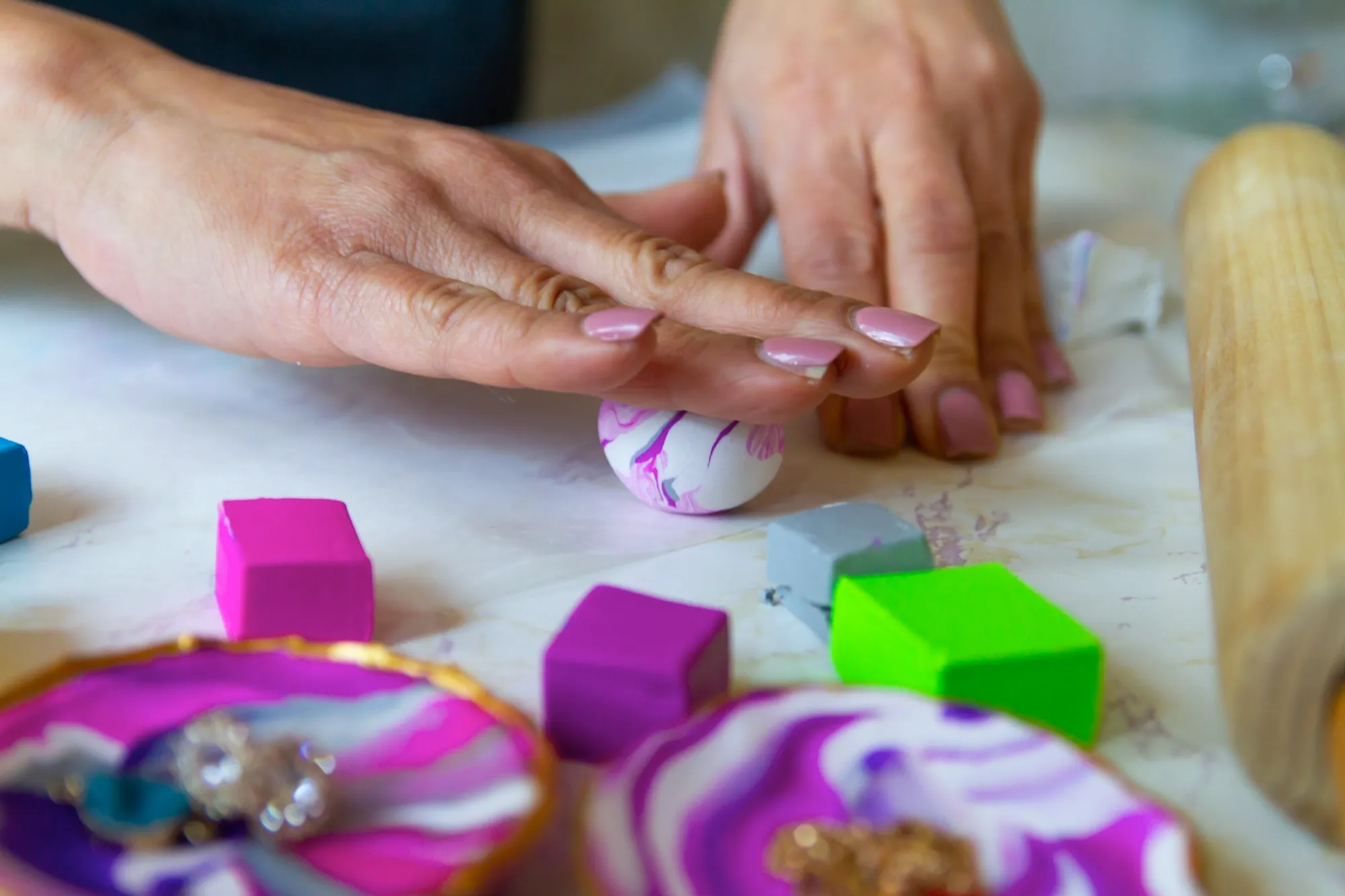 A female hand skillfully crafting and rolling a ball of clay, surrounded by various clay-crafted items such as colorful cubes.