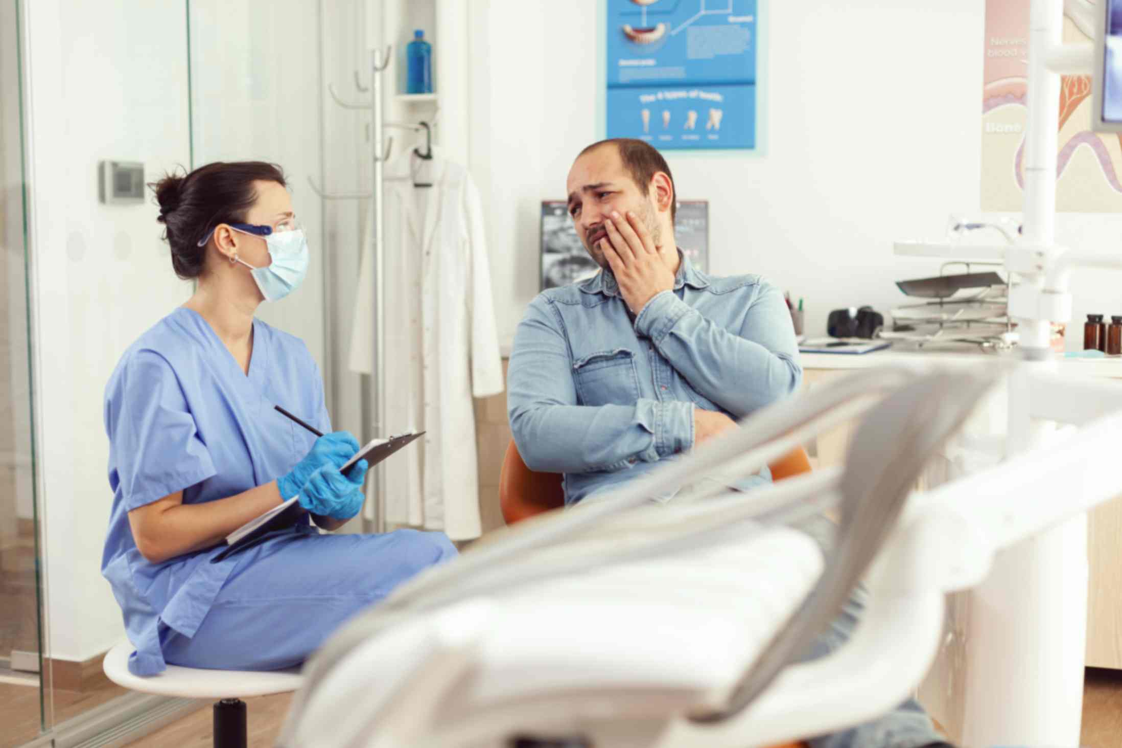 Dental assistant writing stomatology treatment clipboard during sick patient check up