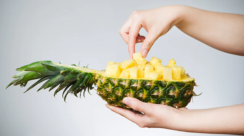 A woman's hand taking out diced pineapple cubes from the fruit's skin