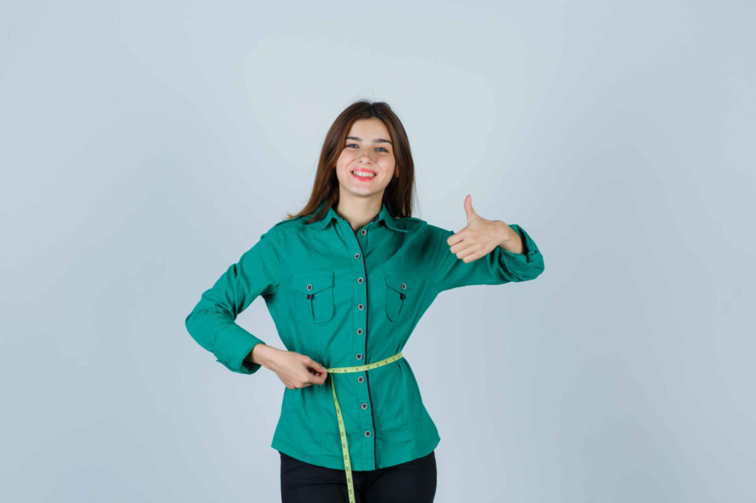 A young girl holding a measuring tape around her waist and raising the thumb of other hand up